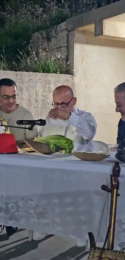 Men seated at a long lace-covered table with microphones