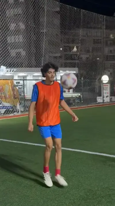 A player in an orange bib keeping the ball up beside his head