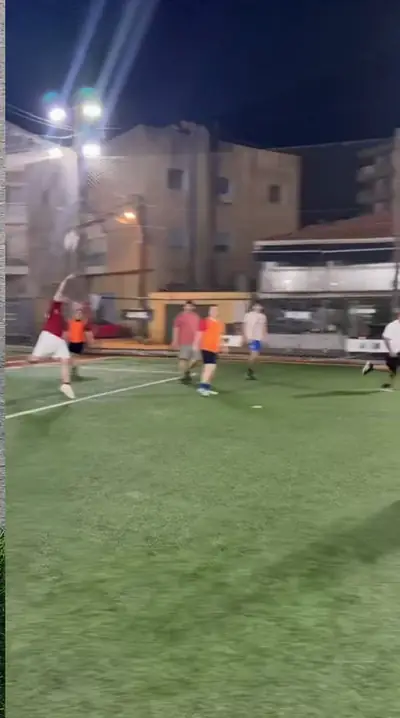 A player striking the ball high across a floodlit pitch