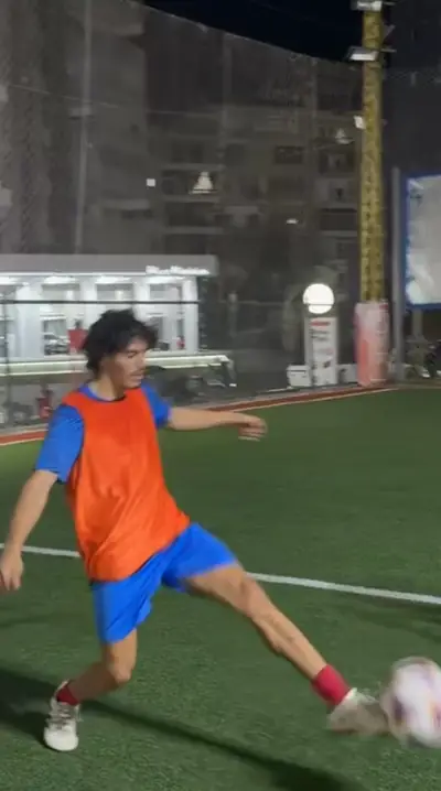 A player in an orange bib stretching to volley the ball