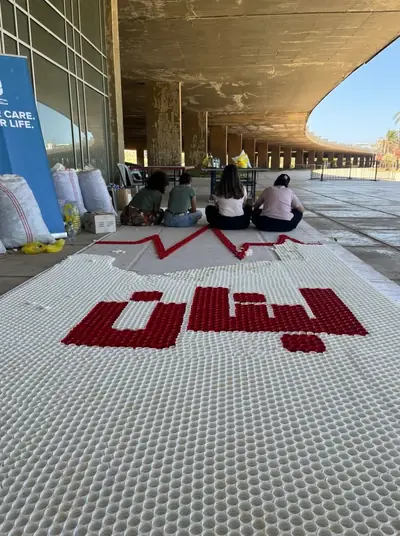 A large bottle-cap mosaic on the ground spelling Lebanon in Arabic