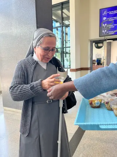 An older woman smiling as a volunteer hands her a cup