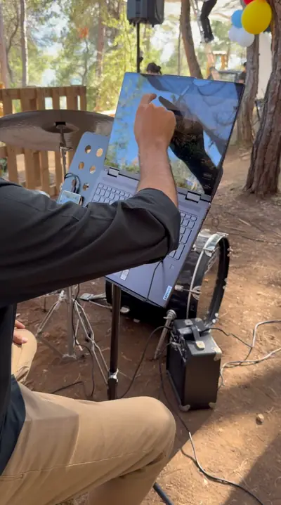 Hands setting up a laptop on a stand beside a drum kit and an amplifier