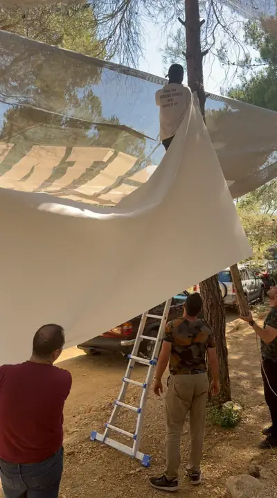 Members hanging a large white screen between pine trees, a ladder below
