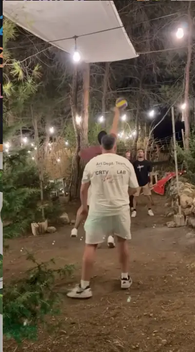 A guest jumping to hit a volleyball under string lights