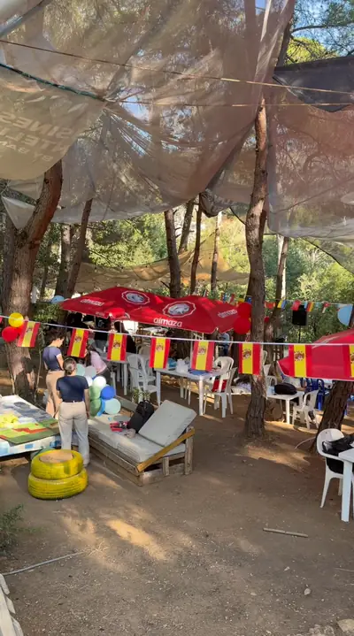 Tables and chairs under strings of flags in the forest, before the guests arrive