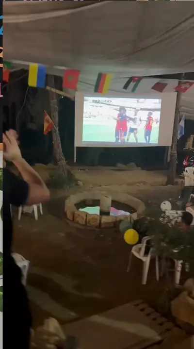The World Cup final playing on an outdoor screen between the pine trees, flags strung overhead